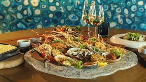 A seafood platter with wine glasses on a table in a restaurant with a blue patterned wall and wooden ceiling. - MARINA SEASIDE BOUTIQUE HOTEL (Phu Quoc)