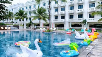Una piscina con flotadores de cisne e flamenco inflables, rodeada de sillas de descanso y palmeras.