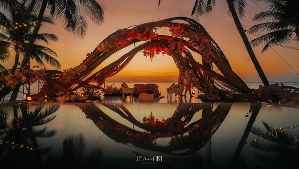 A sunset view with a wooden arch decorated with flowers, palm trees, and a reflective pool. - MARINA SEASIDE BOUTIQUE HOTEL (Phu Quoc)