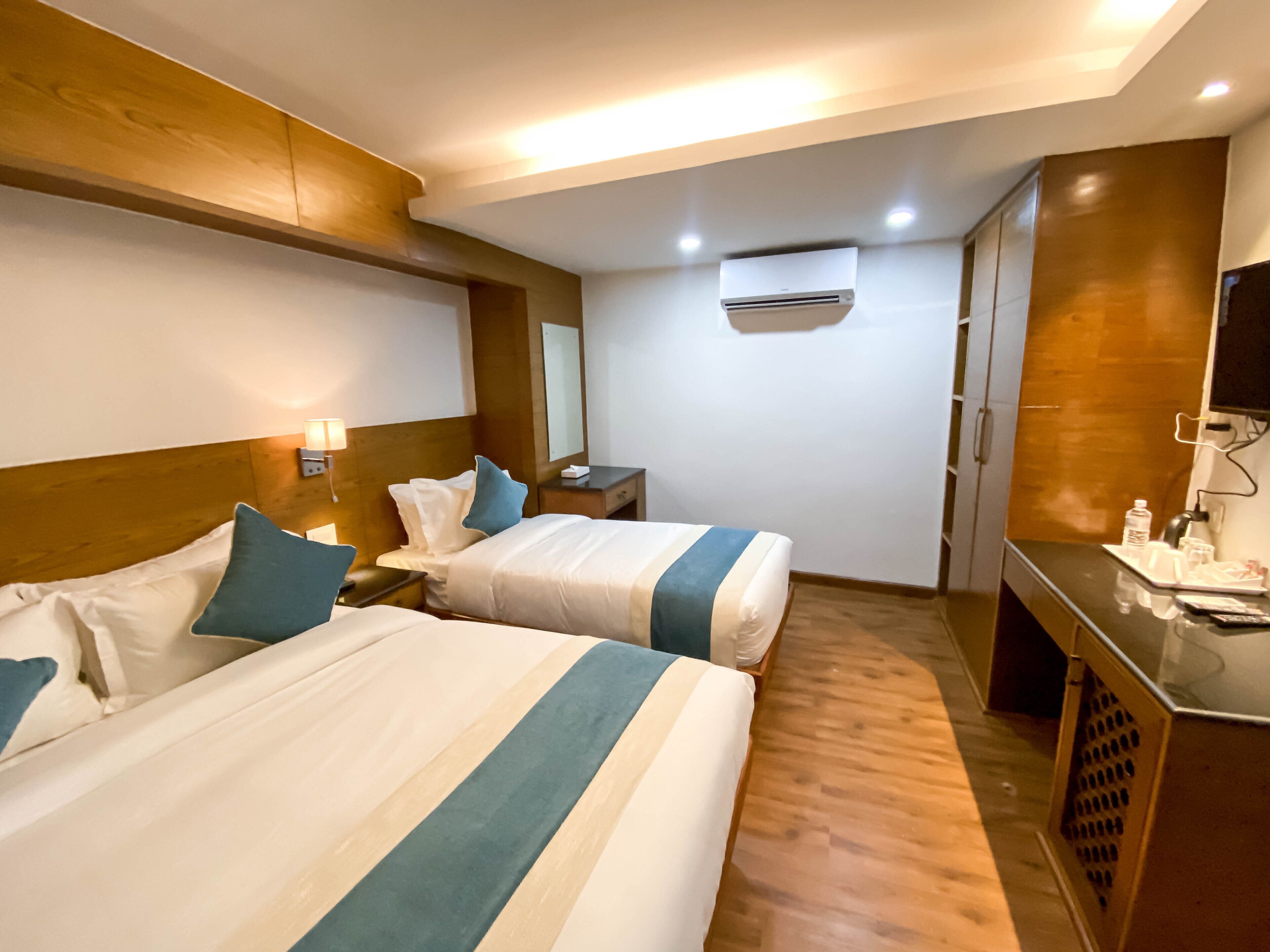 Een hotelkamer met twee bedden, houten hoofdeinden, een flatscreen televisie, een bureau met een stoel en een airconditioner.