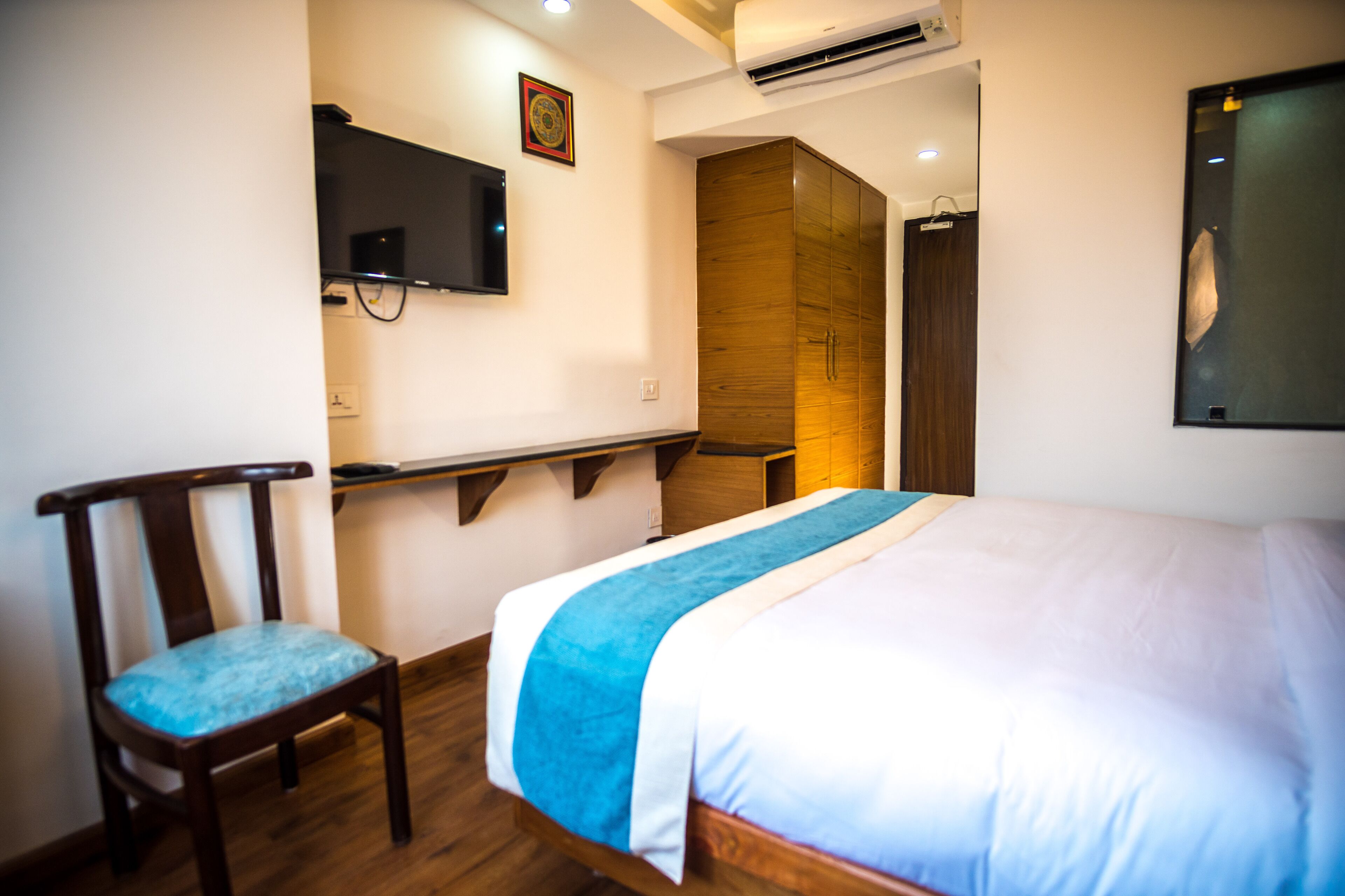 A bedroom with a bed, a chair, a TV mounted on the wall, and a wooden wardrobe.