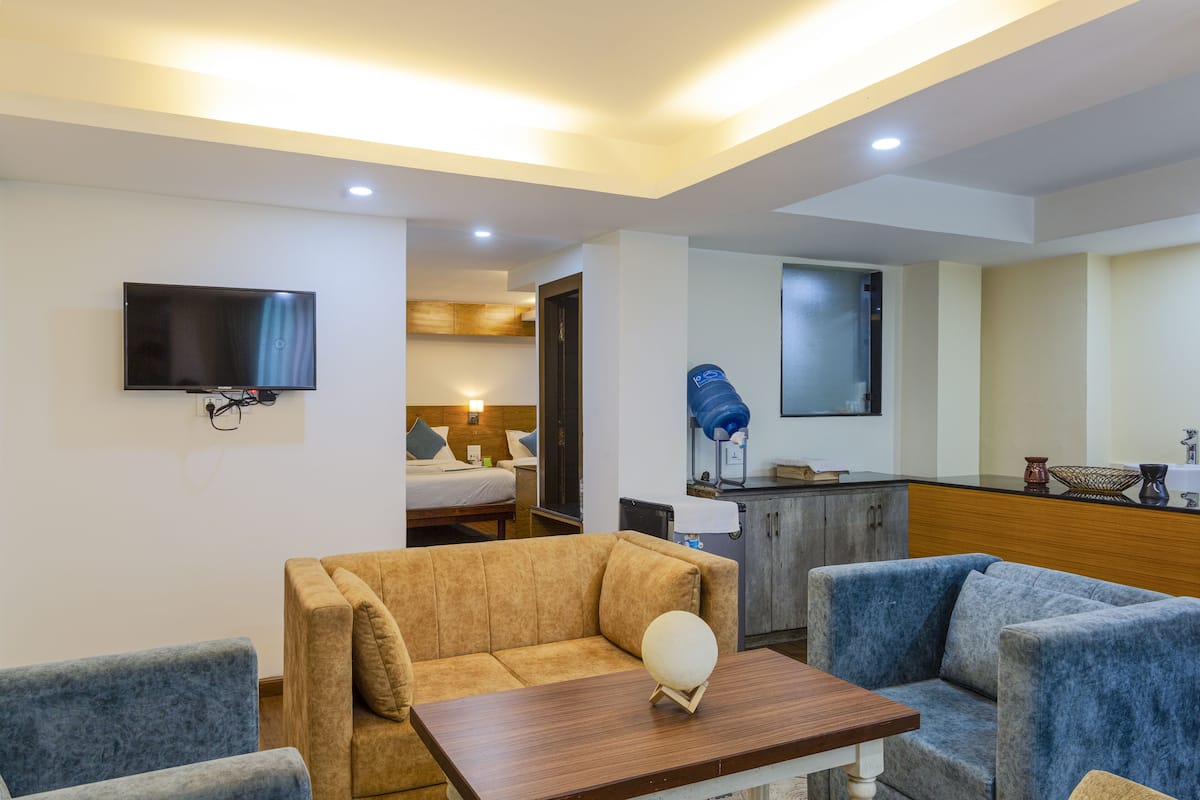 A hotel room with a sofa, a table, a TV, a bed, and a kitchenette.