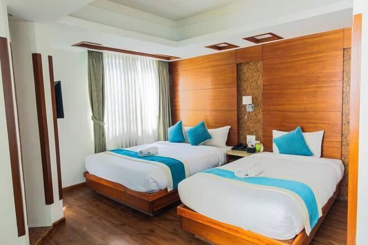A hotel room with two beds, wooden headboards, a nightstand, and a window with curtains.