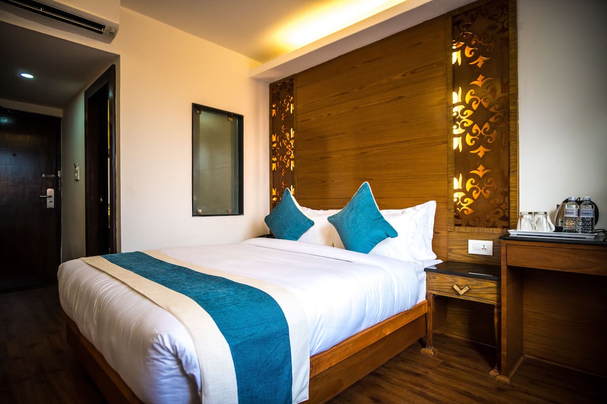 A hotel room with a large bed, wooden headboard, and a nightstand with a lamp and a coffee maker.