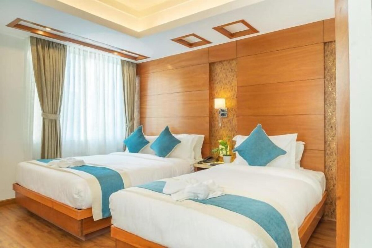 A hotel room with two beds, wooden headboards, a nightstand with a lamp, and a window with curtains.