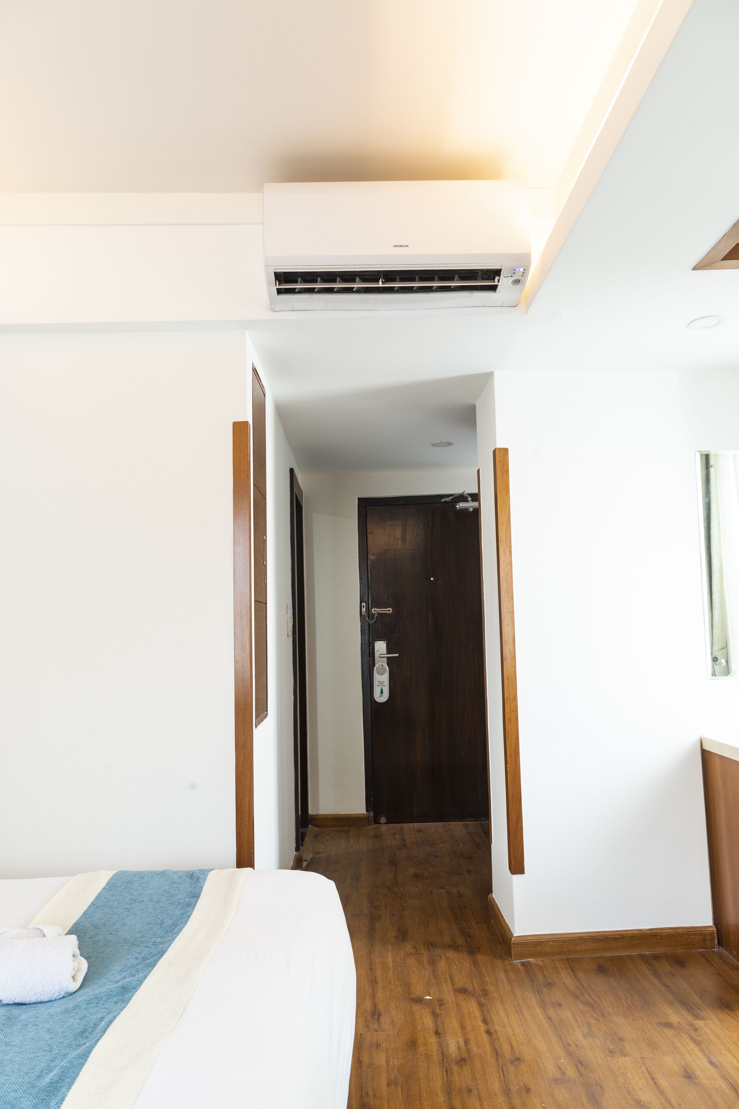 A hotel room with a bed, a wooden floor, a door, and an air conditioning unit.