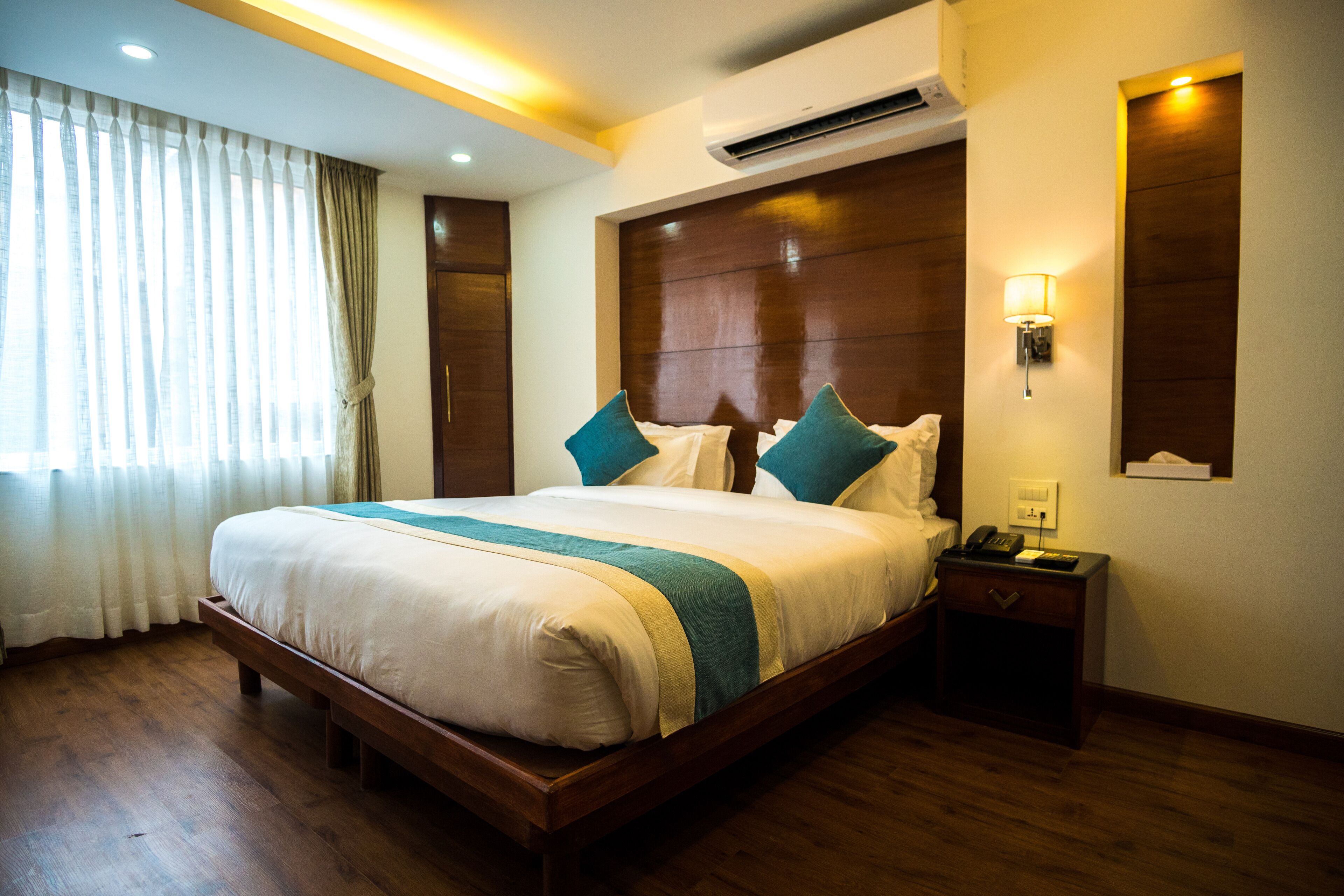 Una habitación de hotel con una cama grande, cabecero de madera, mesita de noche y un pequeño mueble junto a la cama.