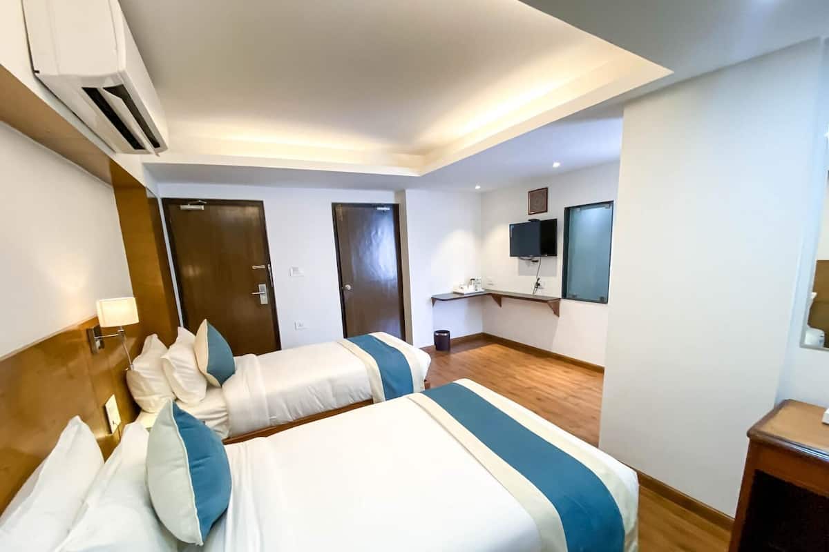 A hotel room with two beds, a desk, a chair, an air conditioning unit, a TV, and a mirror.