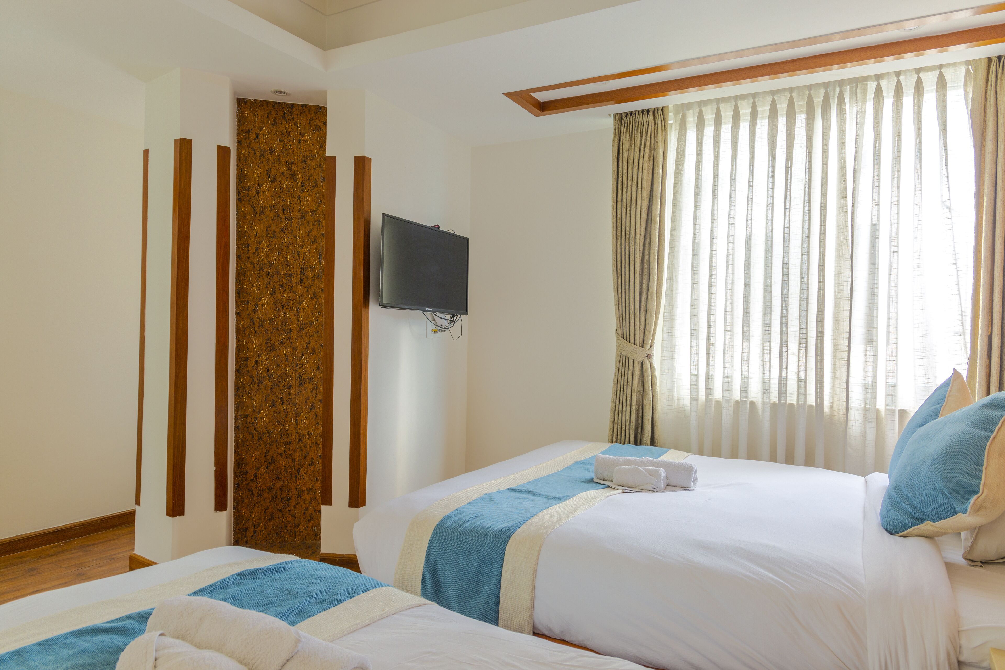 A hotel room with two beds, a television mounted on the wall, and a window with curtains.