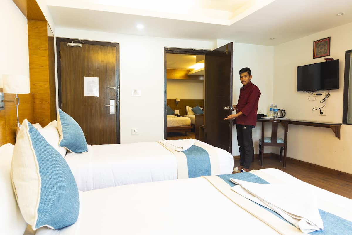 A hotel room with two beds, a desk, a TV, and a door leading to another room.
