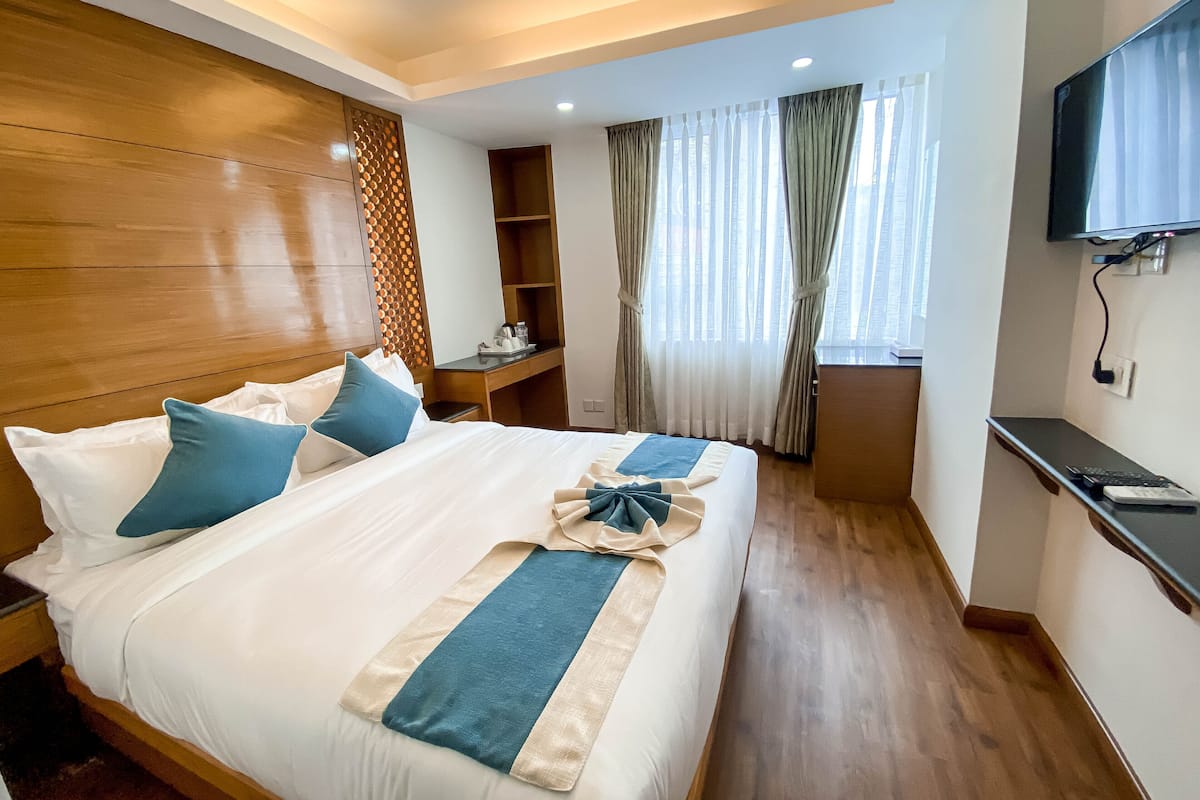 A hotel room with a bed, a desk, a TV, and a window with curtains.