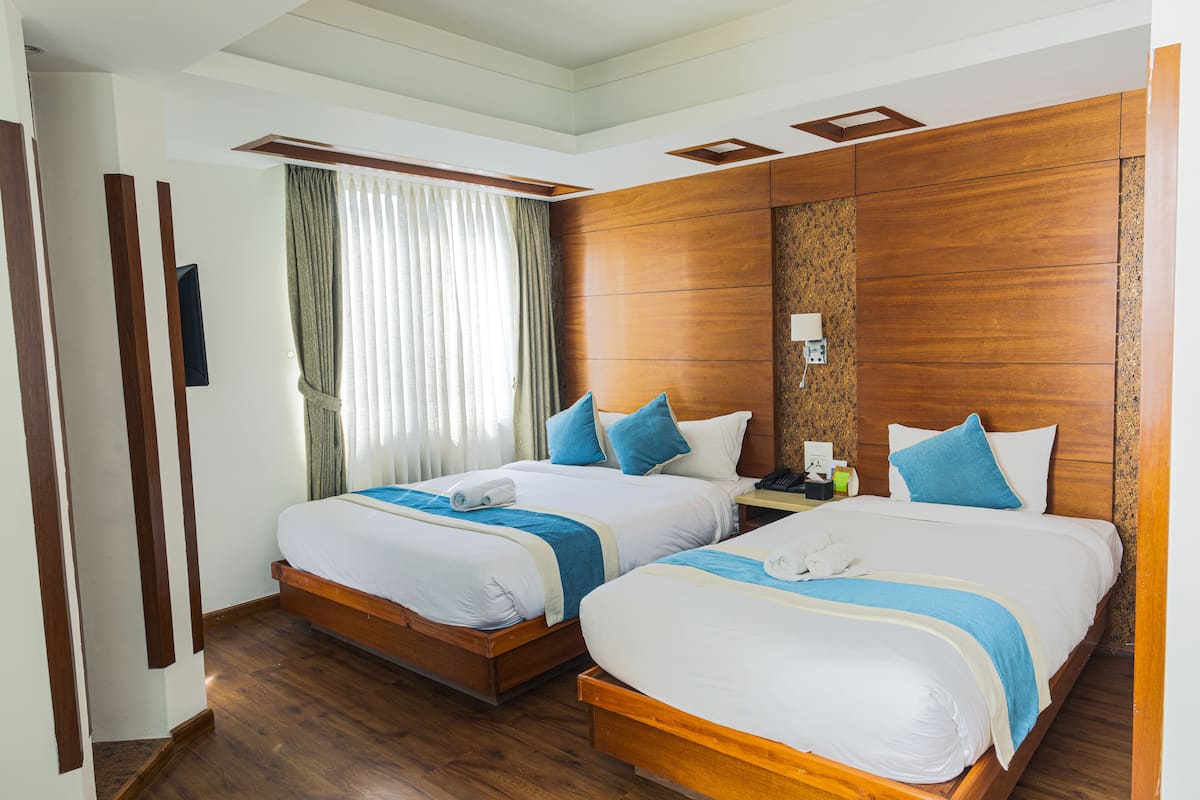 A hotel room with two beds, wooden headboards, and a large window with curtains.