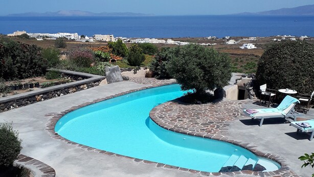 A curved swimming pool with stone edging, surrounded by lounge chairs and a stone patio.