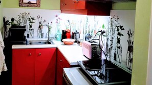 A compact kitchen with red cabinets, a sink, and a stove. There are various kitchen items and plants on the counter.