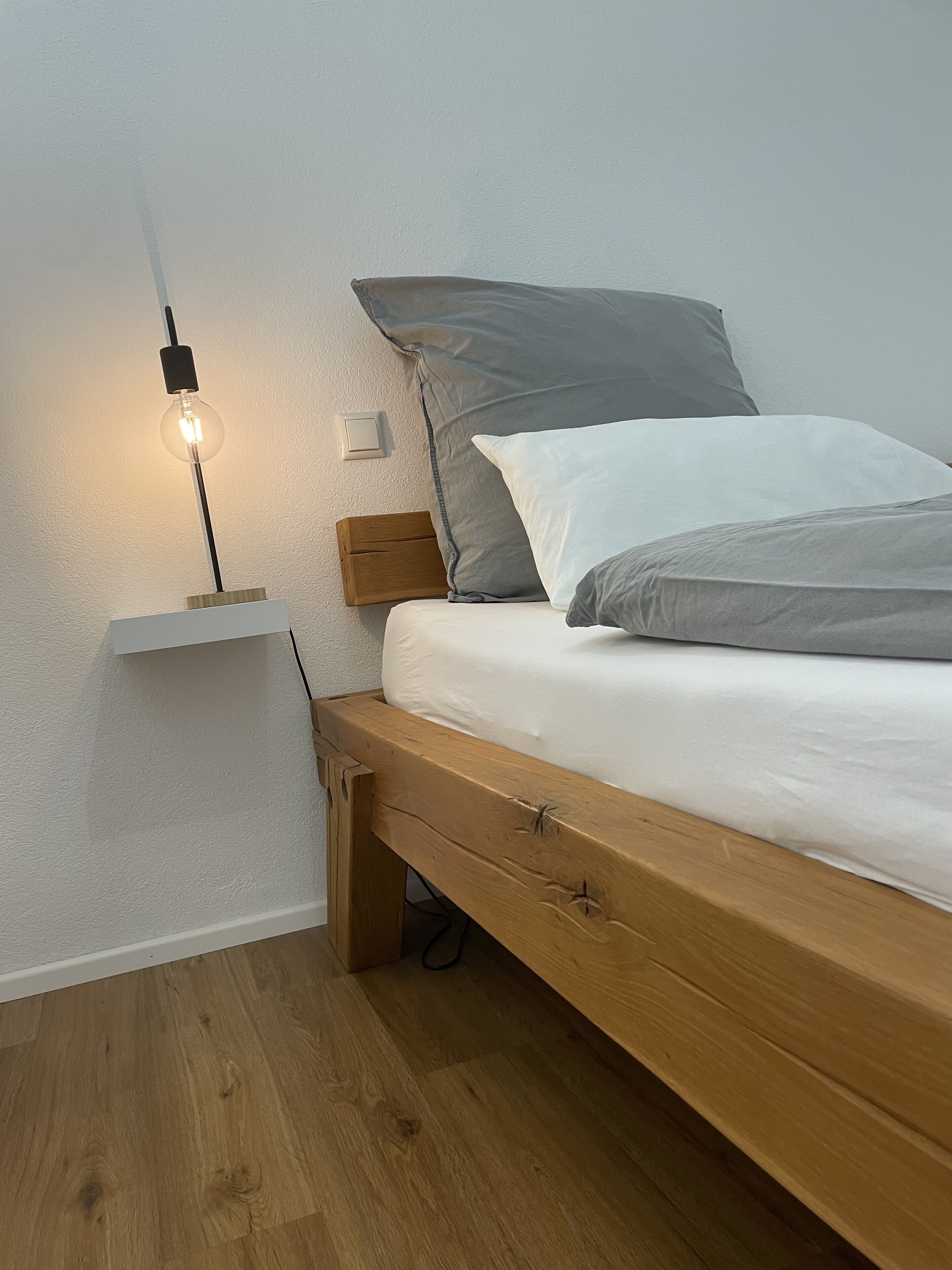 Un lit simple avec un cadre en bois, une table de chevet avec une lampe et un interrupteur mural.