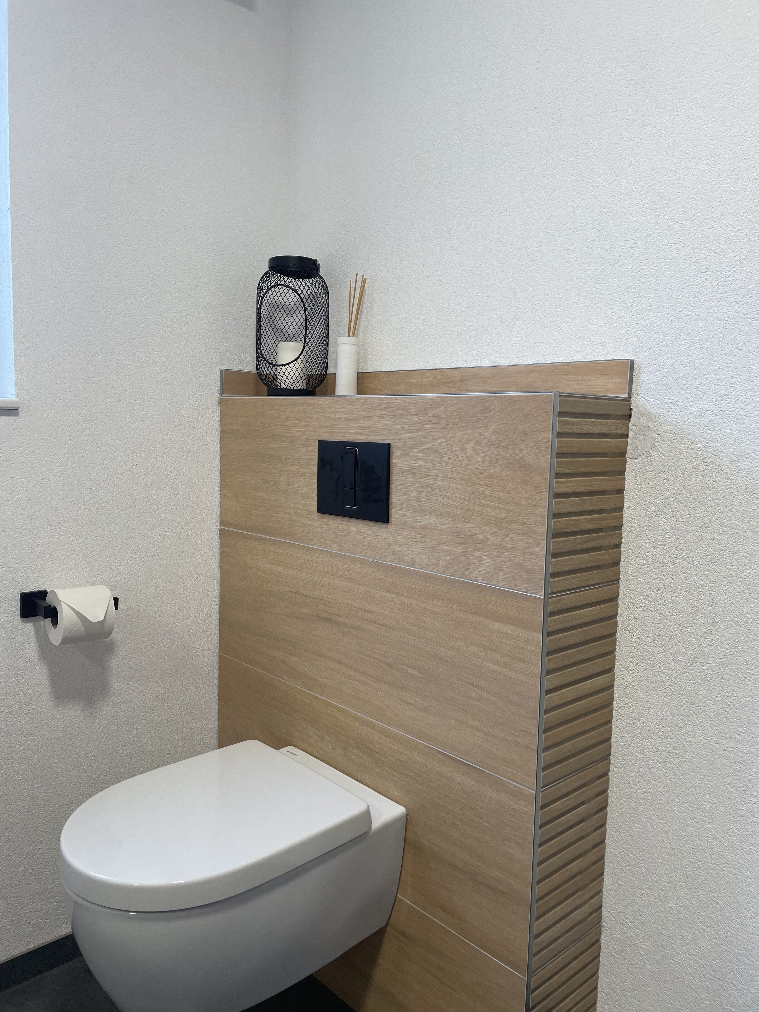 Une salle de bain moderne avec des toilettes blanches, un distributeur de serviettes en papier fixé au mur et un récipient décoratif contenant des bâtonnets.
