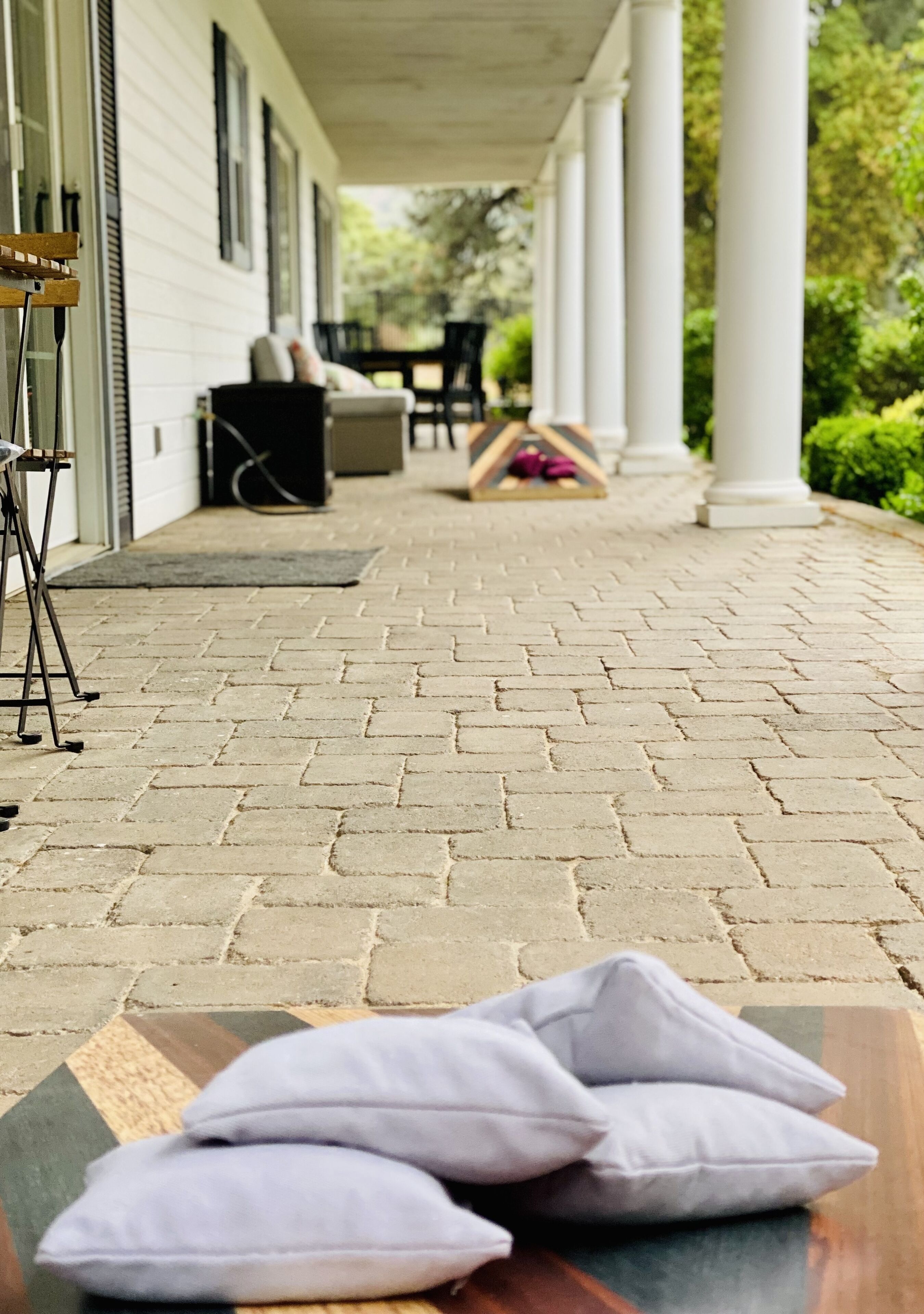 A covered porch with a brick floor, white columns, and outdoor furniture.