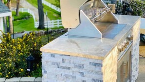 An outdoor barbecue grill with a stone base and a metal lid, set against a backdrop of greenery and a white fence. - Tranquil & clean 5-acre getaway (Grass Valley)