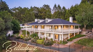 A two-story house with a balcony, surrounded by a stone fence and greenery. - Tranquil & clean 5-acre getaway (Grass Valley)