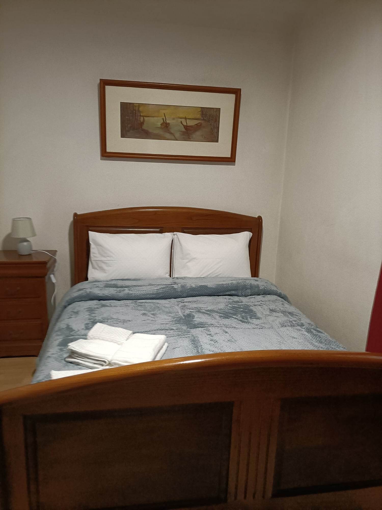 A bedroom with a wooden bed, white pillows, a blue blanket, and a framed picture on the wall.