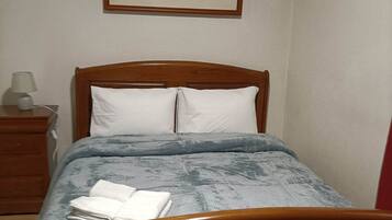 A bedroom with a wooden bed, white pillows, a blue blanket, and a framed picture on the wall.