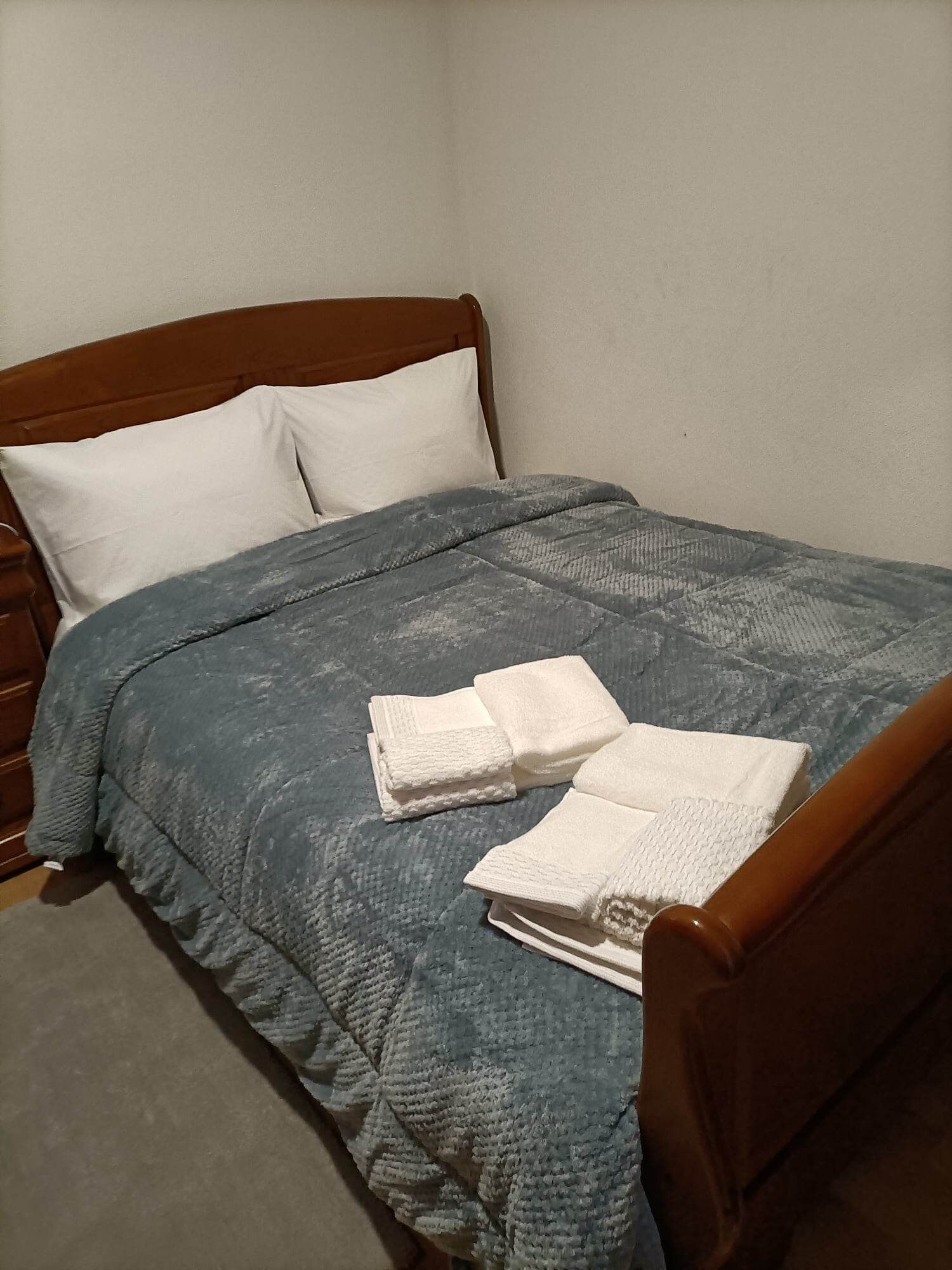 A neatly made bed with a blue blanket, two folded white towels, and a wooden headboard.