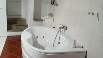 Un baño en esquina con una bañera blanca, una ventana pequeña y piso de azulejos.