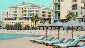 Un hotel frente a la playa con varios balcones, sillas de sol y sombrillas.