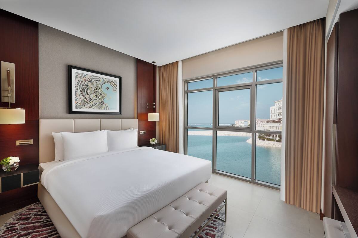 A spacious bedroom with a large bed, a view of the sea, and a framed artwork on the wall.
