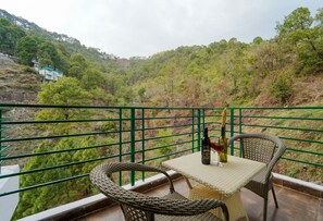 A balcony with wicker chairs and a table, overlooking a lush hillside with a house in the background. - Montrose 11 Boutique (Kasauli)