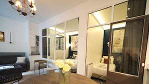 Una habitación de hotel moderna con comedor, sofá, mesa de centro y un florero con flores.