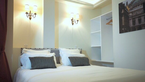 Habitación de hotel con una cama grande, dos apliques, un armario y un cuadro en la pared.