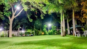 A well-lit outdoor area with a grassy lawn, trees, and a seating area with tables and chairs. - KWETU RESORT (Mtwapa)