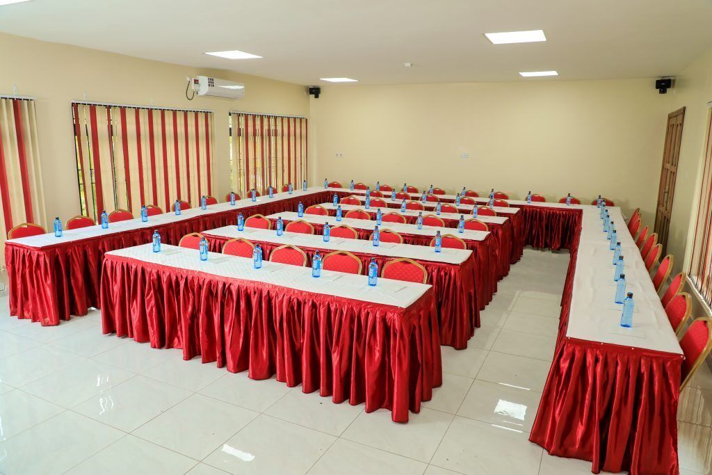 A conference room with multiple tables, red tablecloths, and red chairs.