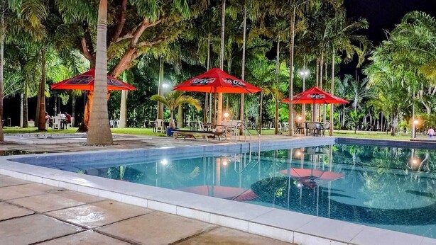 A swimming pool with red umbrellas, surrounded by palm trees and outdoor seating. - KWETU RESORT (Mtwapa)