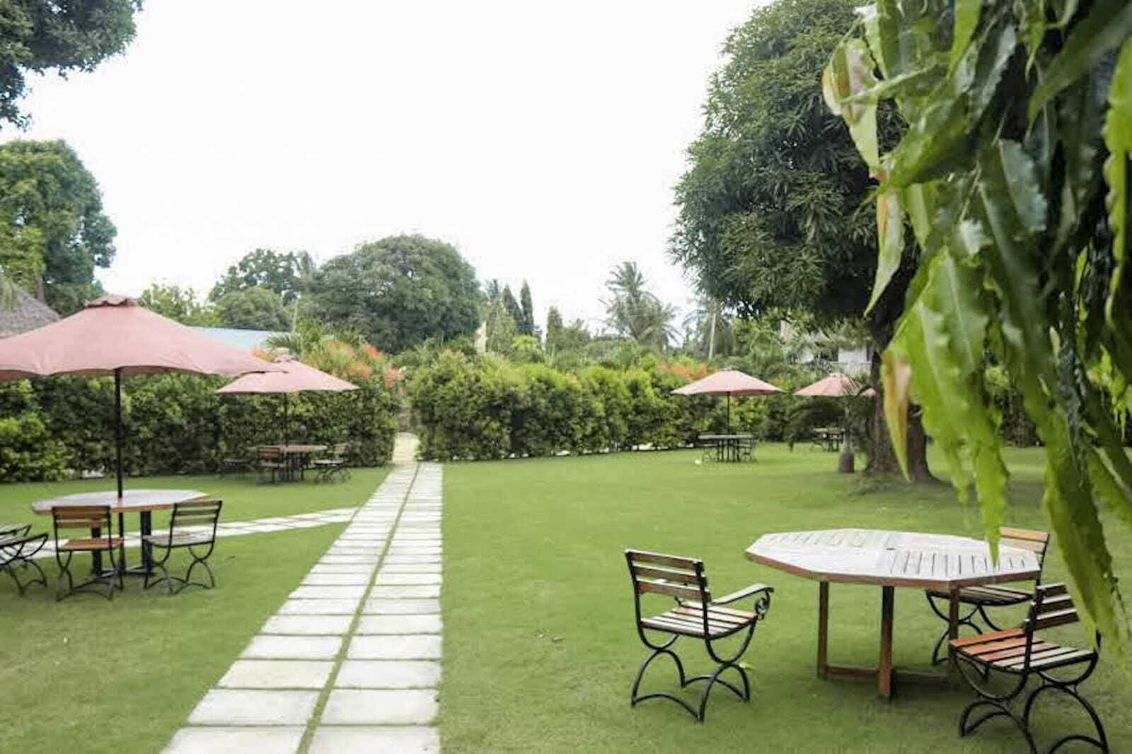 A garden patio with tables and chairs, surrounded by lush greenery and trees.