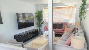 A modern living room with a flat-screen TV, a sofa, a coffee table, and a lamp. - Large House in Bude, Cornwall, Sleep18, Quiet Location, Just 10min Walk To Beach (Bude)