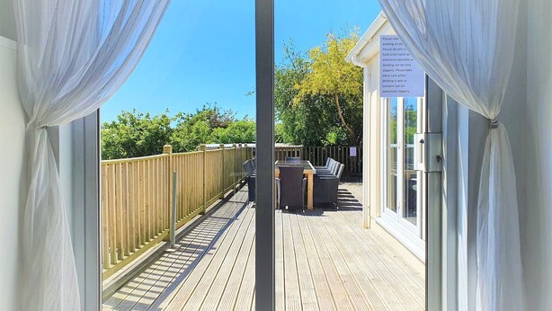 A wooden deck with a table and chairs, a wooden fence, and a building with a sign. - Large House in Bude, Cornwall, Sleep18, Quiet Location, Just 10min Walk To Beach (Bude)