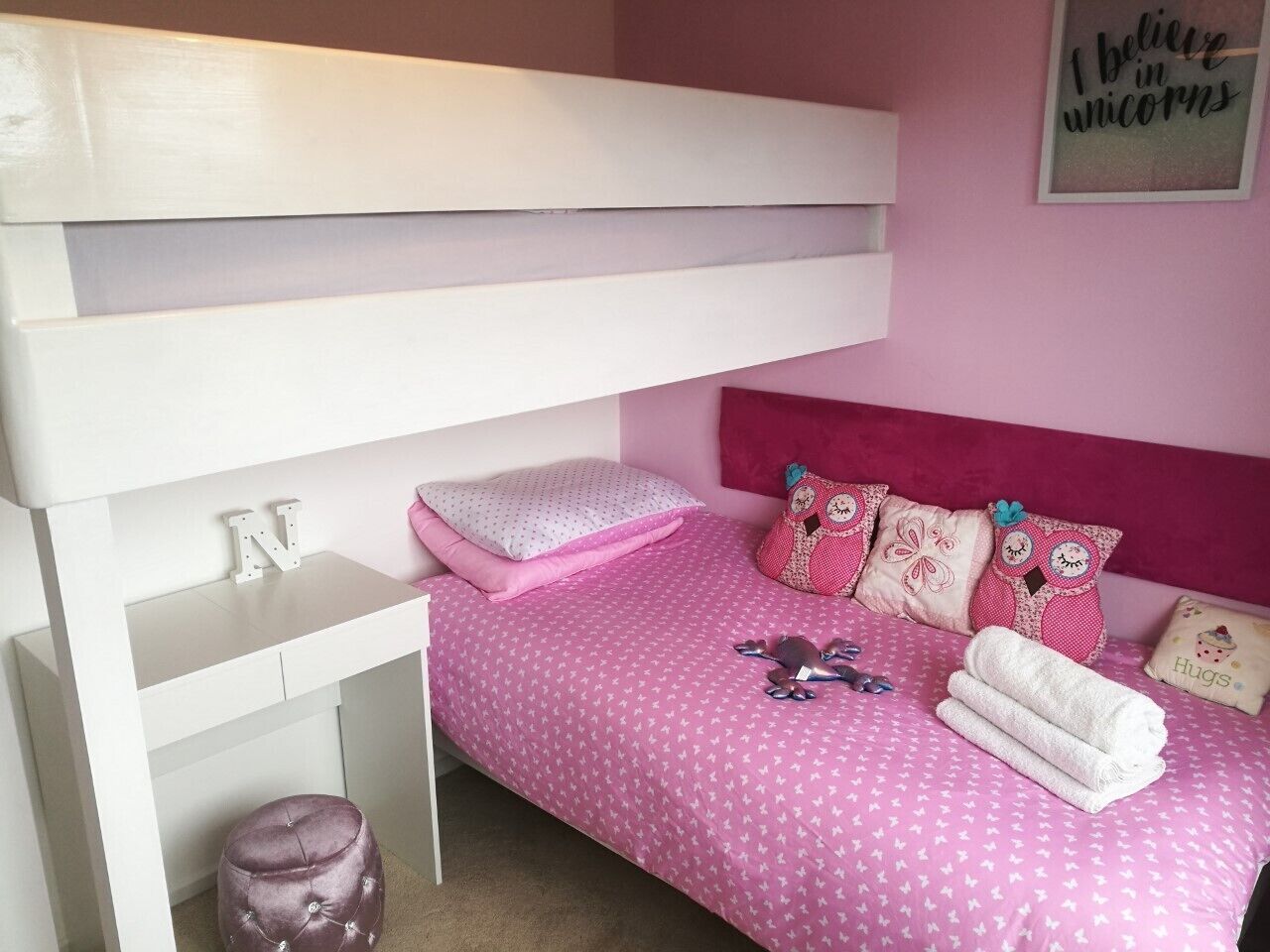 A pink-themed bedroom with a bunk bed, a small desk, and decorative pillows.