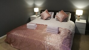 A neatly made bed with a patterned bedspread and pillows, two bedside lamps, and a small white nightstand. - Large House in Bude, Cornwall, Sleep18, Quiet Location, Just 10min Walk To Beach (Bude)