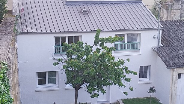 A white building with a metal roof, multiple windows, and a tree in the front yard. - House in historic center of Caen! (Caen)