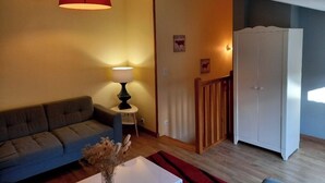 A living room with a sofa, a table with a lamp, a red hanging light, a white wardrobe, and a staircase. - House in historic center of Caen! (Caen)