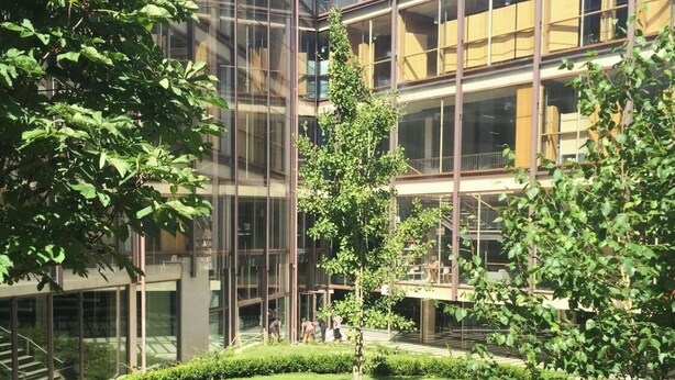 Ein modernes Gebäude mit großen Glasfenstern und einem gepflegten Innenhof mit Rasen und Bäumen.