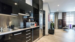 Eine moderne Küche mit Edelstahlgeräten, einem Backofen und einer Mikrowelle. Ein Spülbecken mit Wasserhahn ist vorhanden, und die Küche verfügt über dunkle Schränke mit silbernen Griffen.