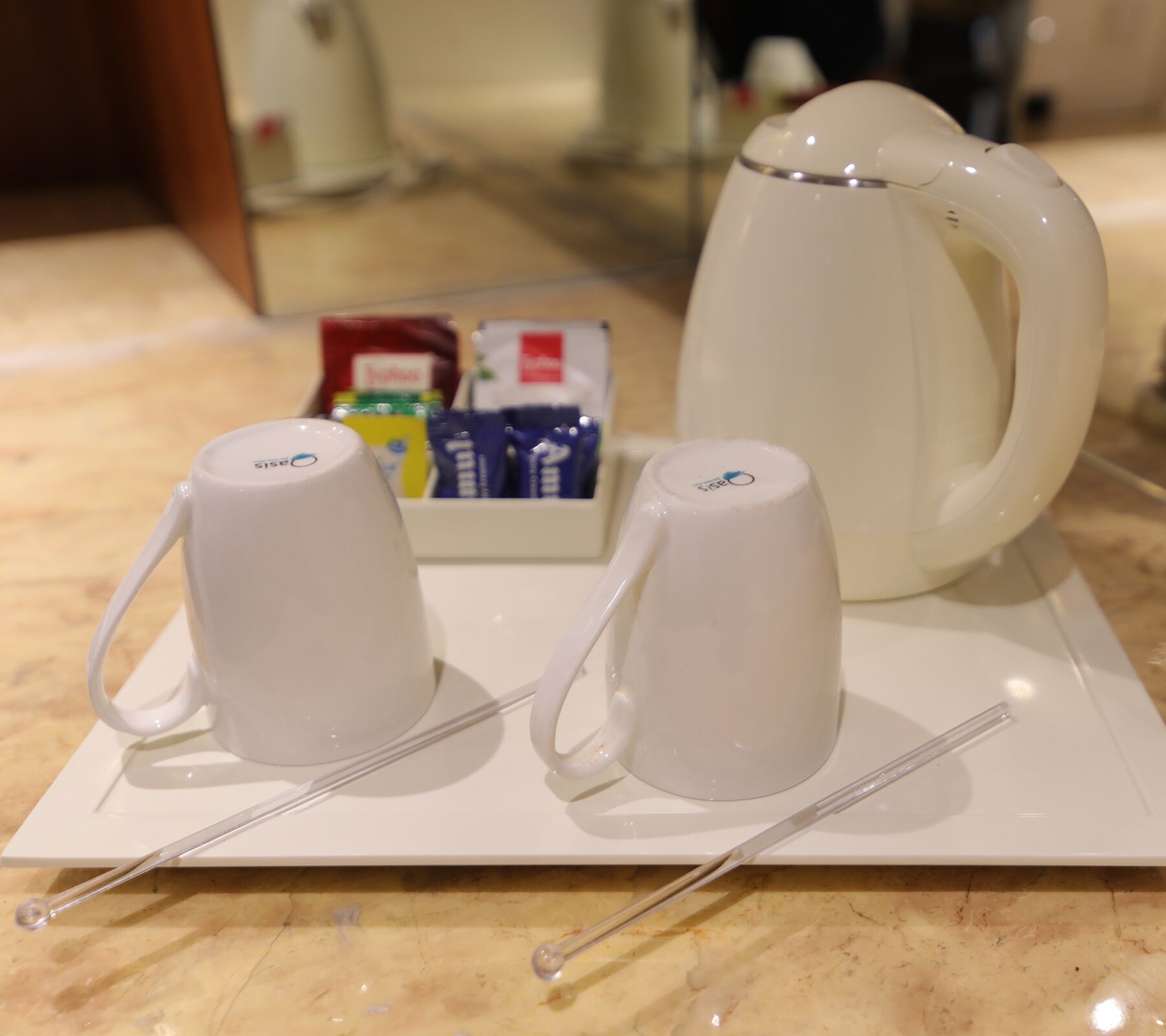 A white electric kettle, two white cups, and a tray with a box of tea bags on a marble countertop.
