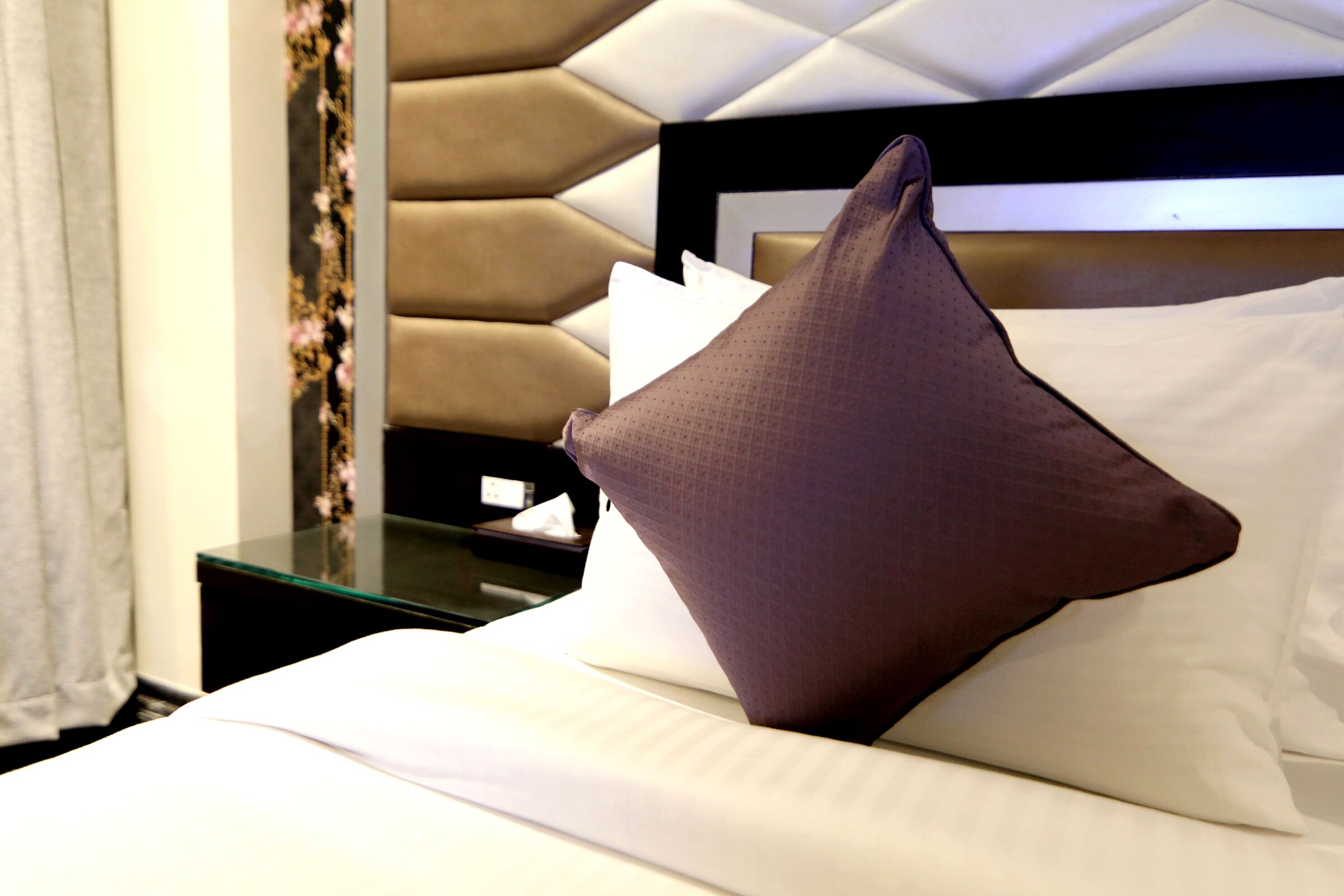 A neatly made bed with a brown pillow and white linens.