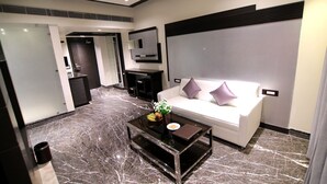 Een moderne hotel lobby met een marmeren vloer, een witte bank met paarse kussens, een bijzettafeltje met een bloemenvaas, en een zwarte entertainmentkast.