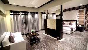 Een moderne hotelkamer met een marmeren vloer, een witte bank met kussens, een klein tafeltje met een vaas en een bed met hoofdbord en kussens.