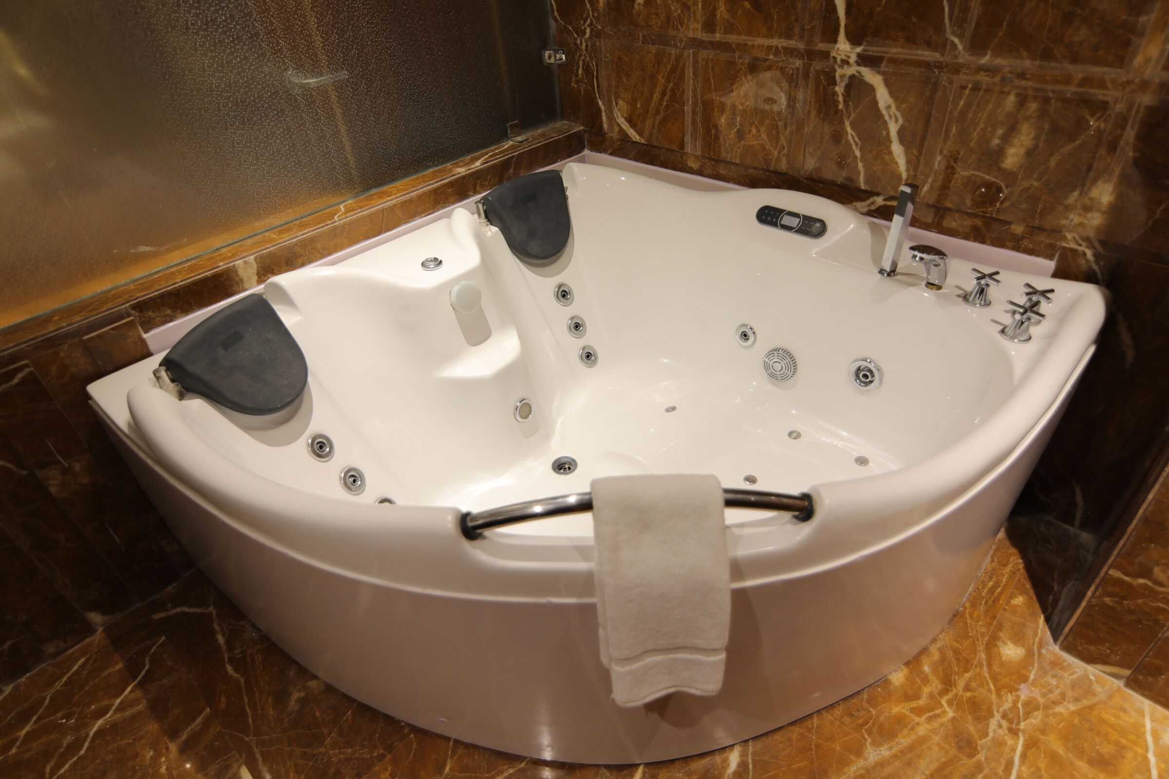 A large, oval-shaped bathtub with a built-in seat and control panel, set against a marble wall.