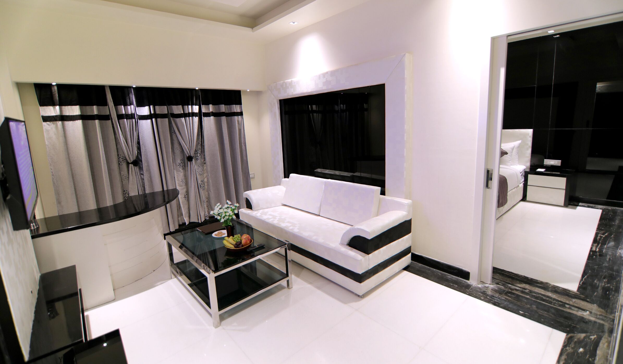 A modern living room with a white sofa, a glass coffee table, and a black and white striped wall.